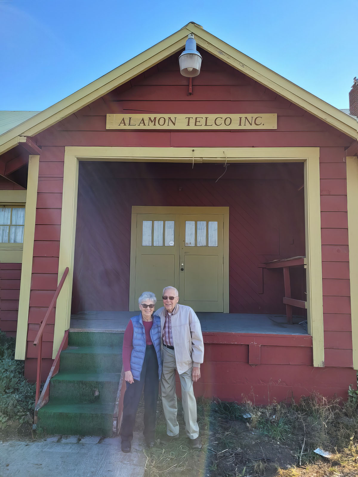Peg and Frank Gebhardt stand in front of the first home of Alamon Telco, Inc. (the former Sunrift Hall)